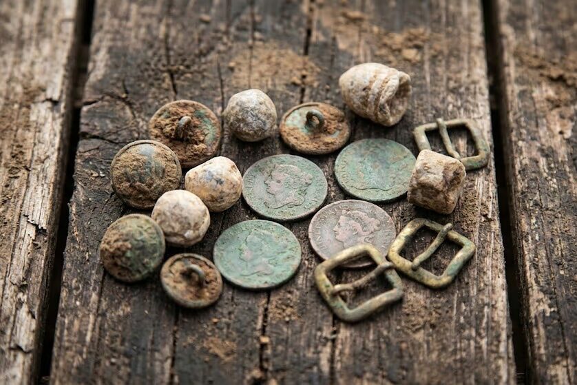 Authentic civil war relics and colonial coins displayed on weathered wood showing metal detecting finds from relic hunting