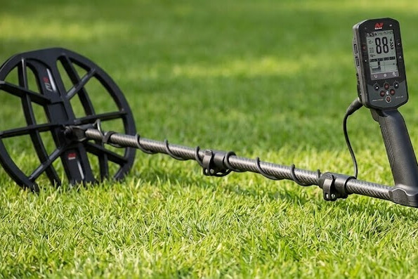 Minelab Manticore multi-frequency metal detector with carbon fiber shaft and M11 coil shown on grass with wireless headphones