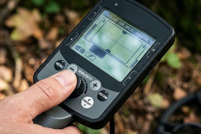 Close up of metal detector control panel showing digital display settings for sensitivity and ground balance adjustments